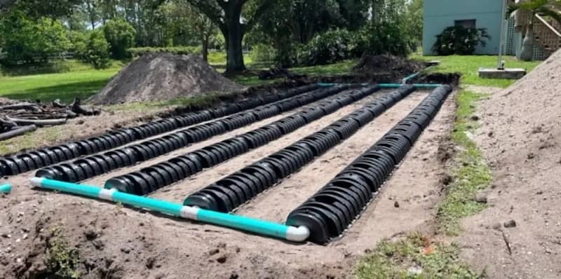 Completed leach field installation with infiltrator chambers and teal PVC pipes, ready for backfill